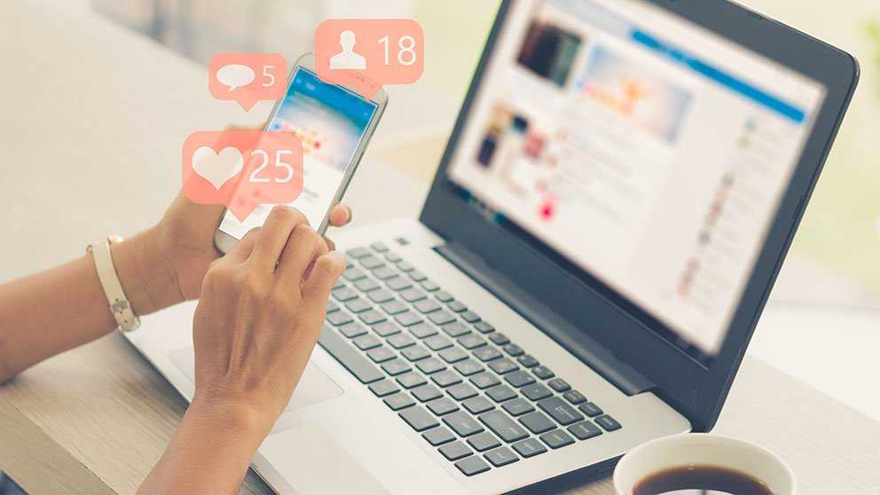 Laptop and phone both open, posting to social media platform, getting likes and comments